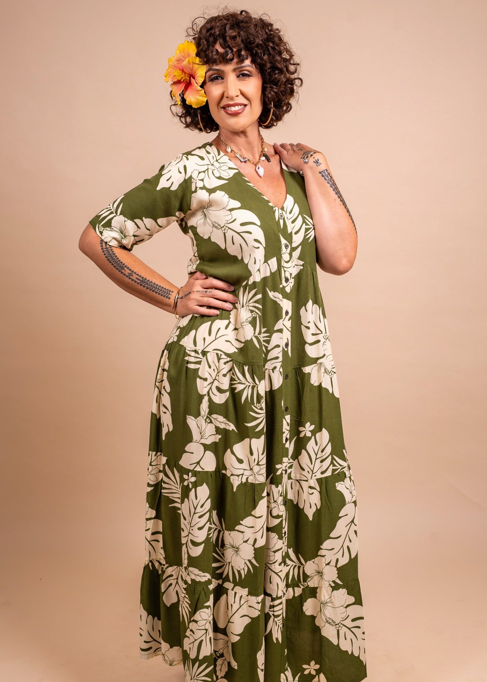 Tattoo Women with a beautiful yellow hibiscus on her ear wearing a long polynesian dress in green olive color with hibiscus pattern