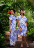 Deux femmes portant la robe La Tevahine de Bamboo Kultur, modèle polynésien lavande à motifs fleuris avec détails en dentelle, dans un décor tropical.