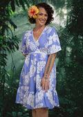 Woman wearing a lavender Polynesian floral Bamboo Kultur short  dress,  with a hibiscus in their hair.
