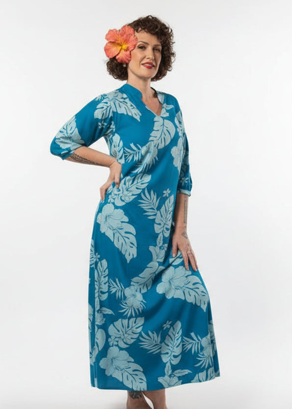 Woman wearing Bamboo Kultur’s Mihivai model in blue Polynesian floral pattern, in a tropical setting.