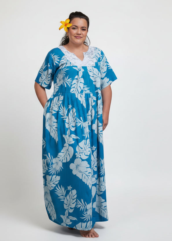 Woman wearing Bamboo Kultur’s Poema model in a long lace-detailed dress blue Polynesian floral pattern, in a tropical setting.