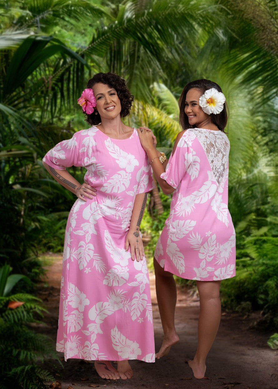 Two women wearing Bamboo Kultur’s “La Teavei” pink floral Polynesian dresses with V lace details, standing in a tropical setting.