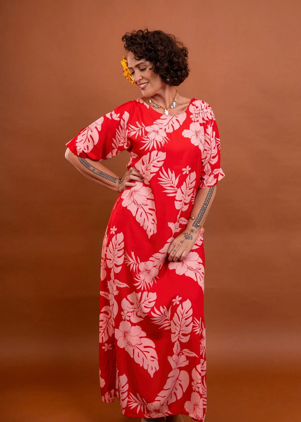 Women with tattoo wearing a long polynesian dress in cherry tomato color with hibiscus pattern
