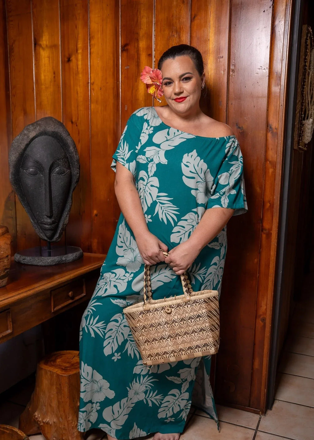 Women with a beautiful red hibiscus on her ear wearing a long polynesian dress in green emeraude color with hibiscus pattern