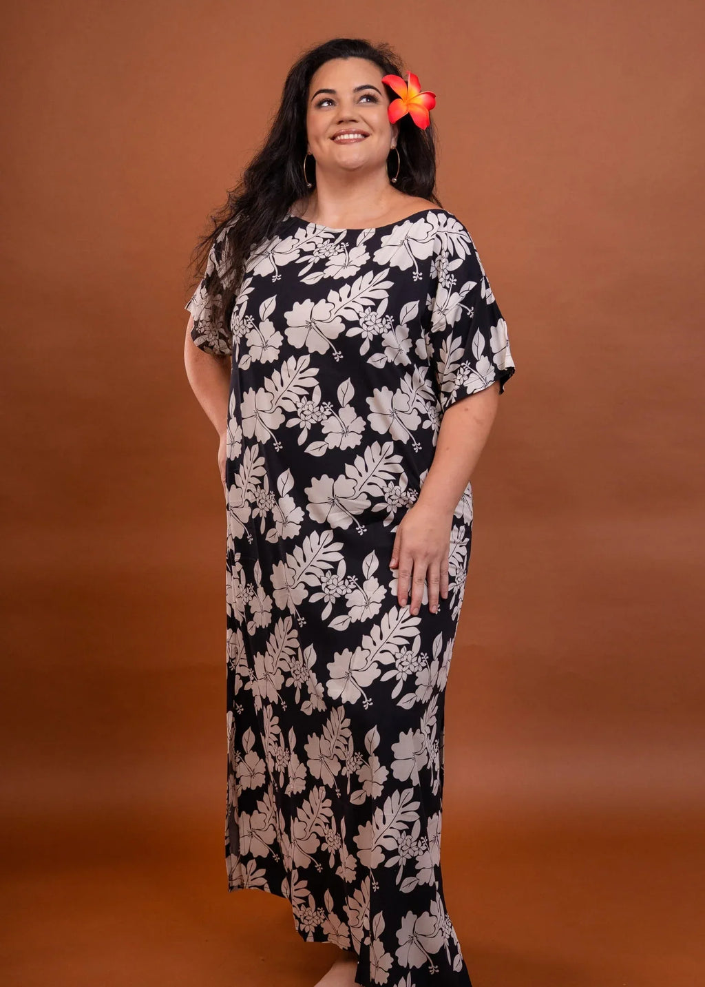 Women with a beautiful red hibiscus on her ear wearing a long polynesian dress in dark color with hibiscus pattern
