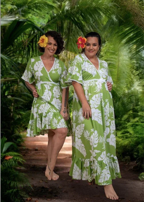 Two woman wearing a green Polynesian floral Bamboo Kultur short and long dress,  with a hibiscus in their hair.